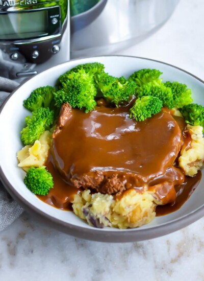 Cube steak with gravy in a bowl with broccoli and mashed potatoes.