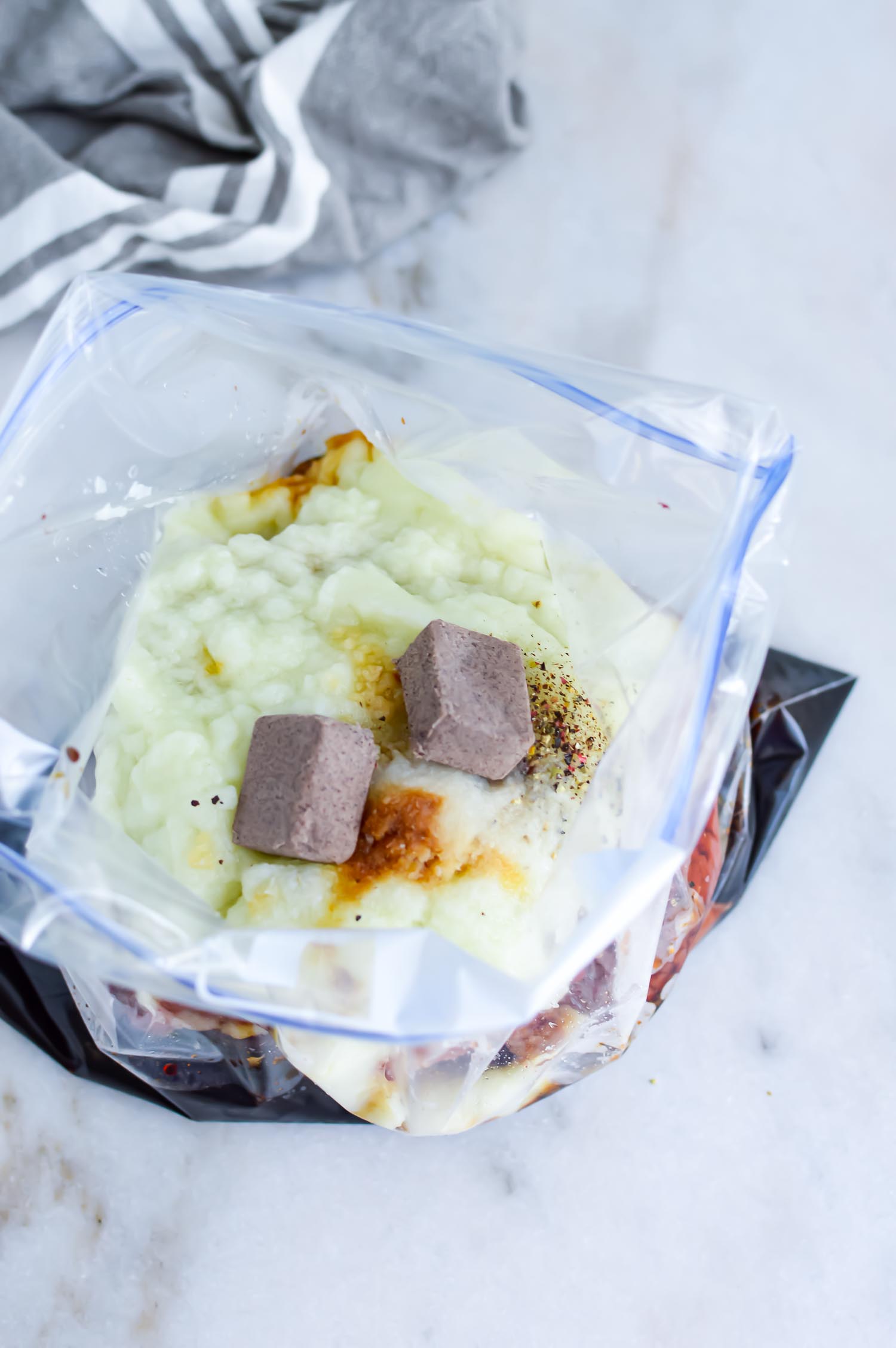An open gallon resealable bag with potatoes, meat, seasoning cubes and spices in it.