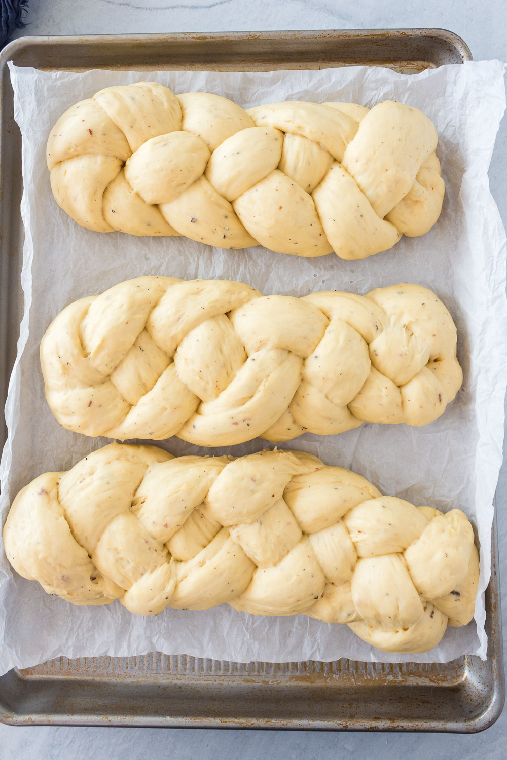 Three unbaked loafs of braided bread on a cookie sheet.