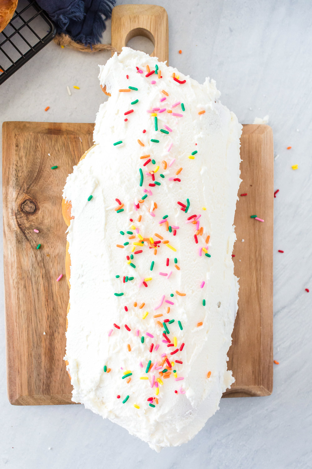 An iced with sprinkles loaf of cardamom bread on a wooden cutting board.
