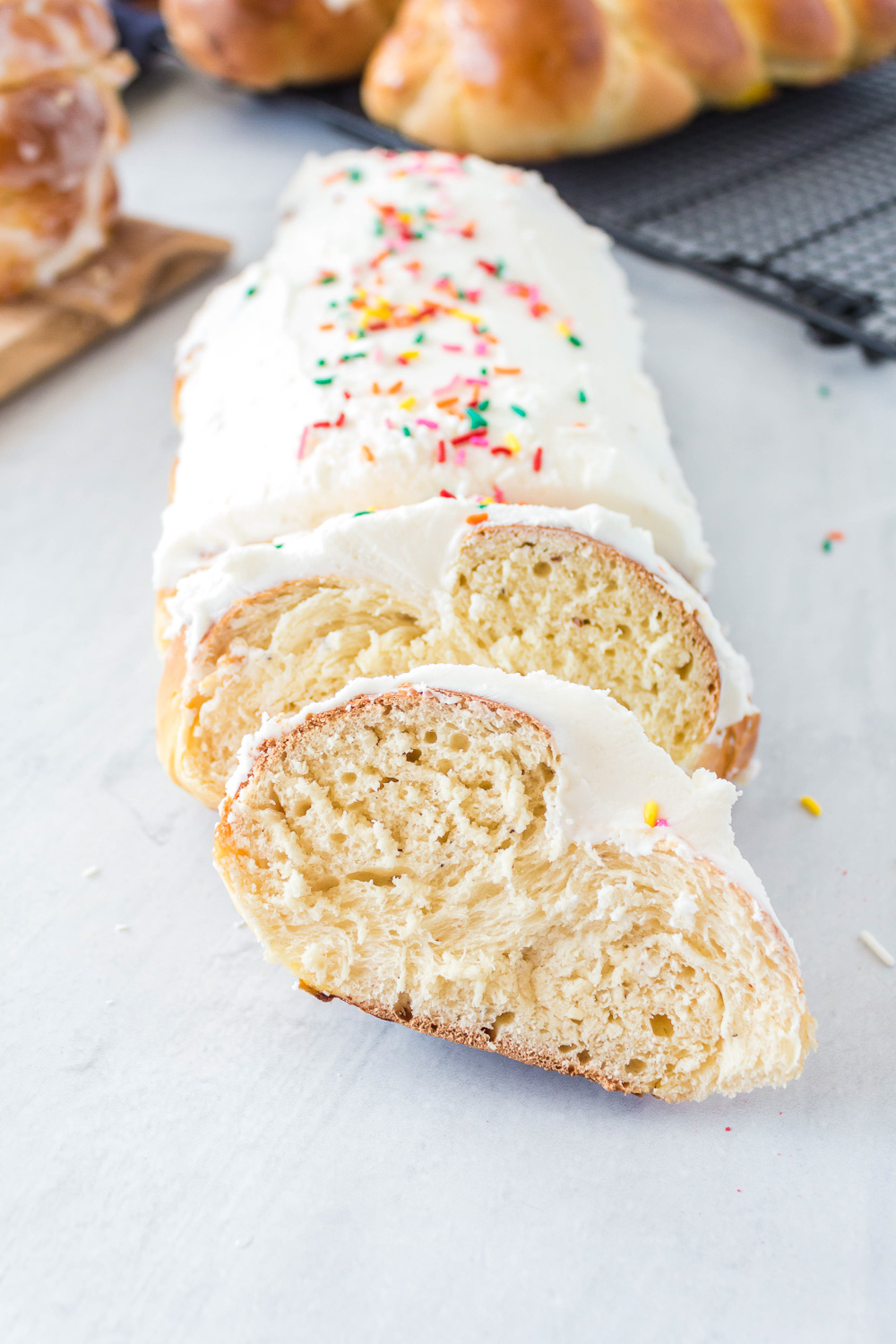 An iced with sprinkles loaf of bread with two pieces cut and laying back on the bread on a white counter.