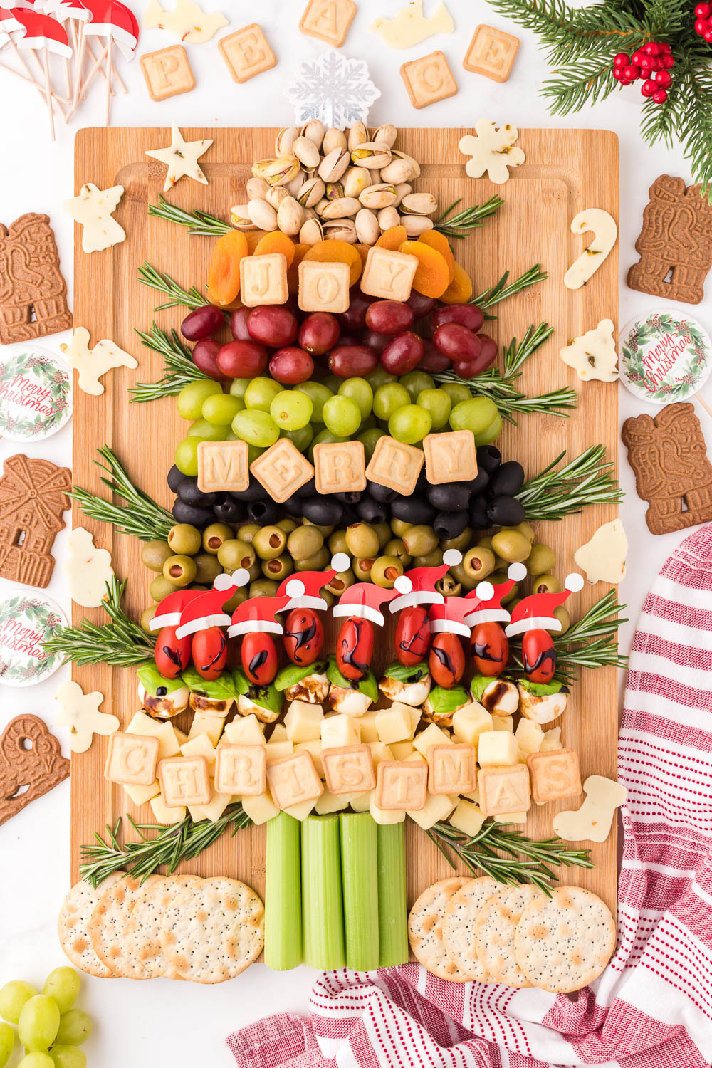 A wooden board with snacks, fruits and food in the shape of a Christmas tree with cookies and signs around it.