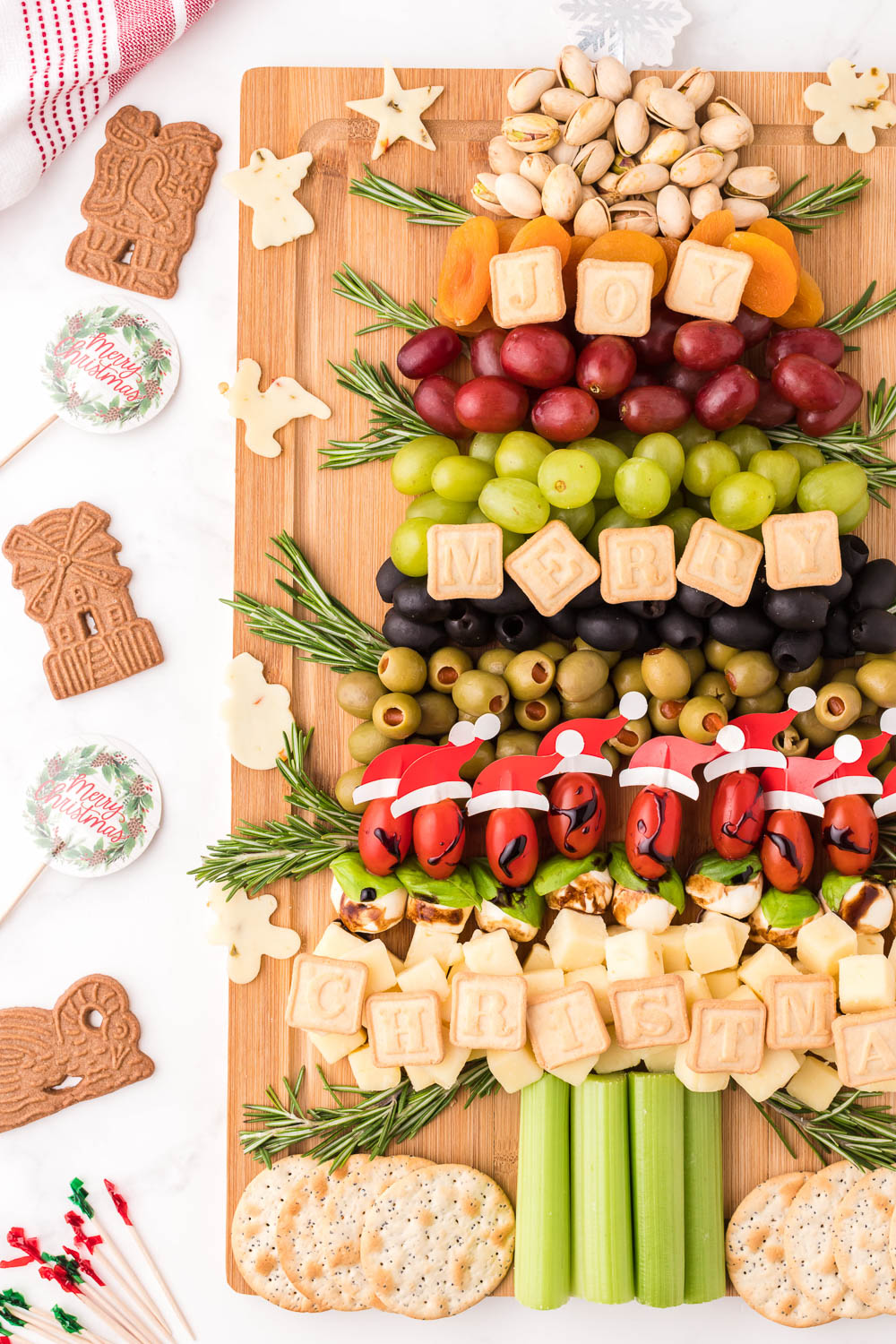 A wooden board with snacks, fruits and food in the shape of a Christmas tree with cookies and signs on the side.
