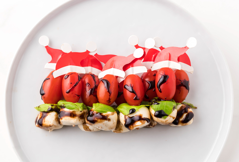 A white plate with caprese skewers with Santa hats on them.