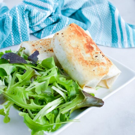 Chicken burrito on a plate with a salad.