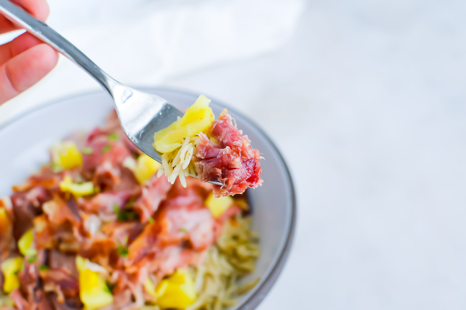 A bowl of shredded meat with bacon and pineapple with a fork held up with a bite of the food.