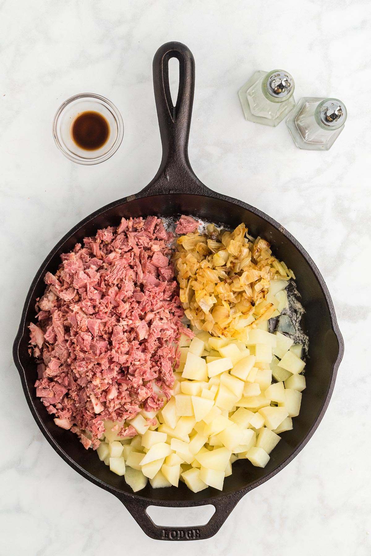 A black skillet with cut potatoes, corned beef, and onions in it.