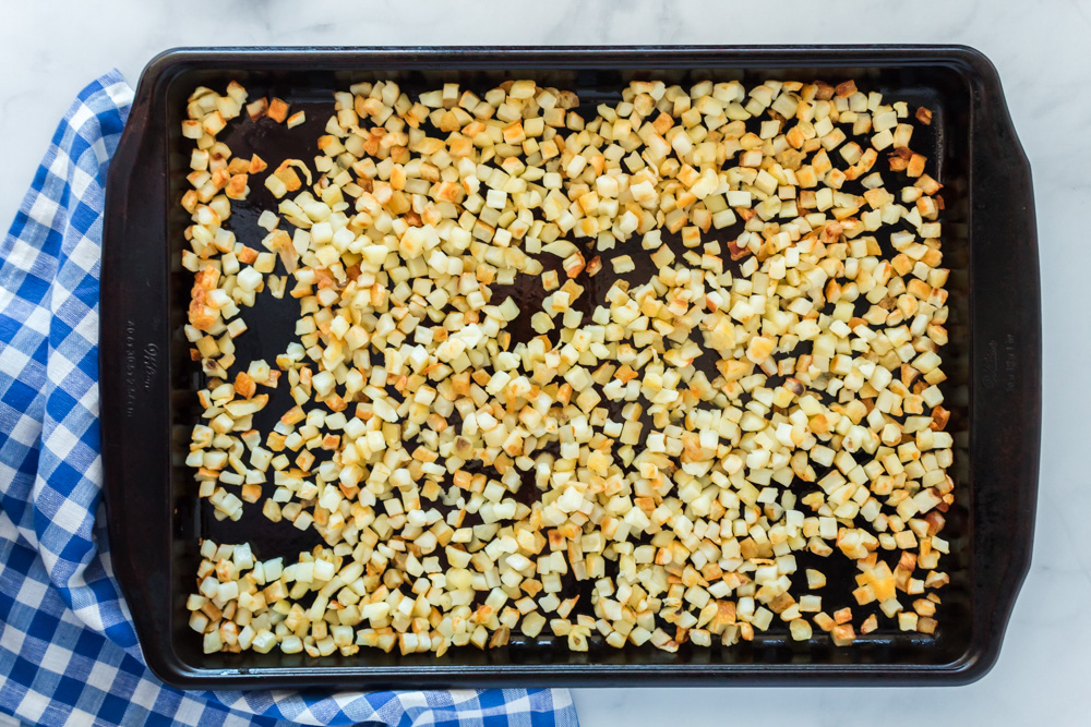 A sheet pan with crispy hash browns with a blue and white checked towel underneath it.