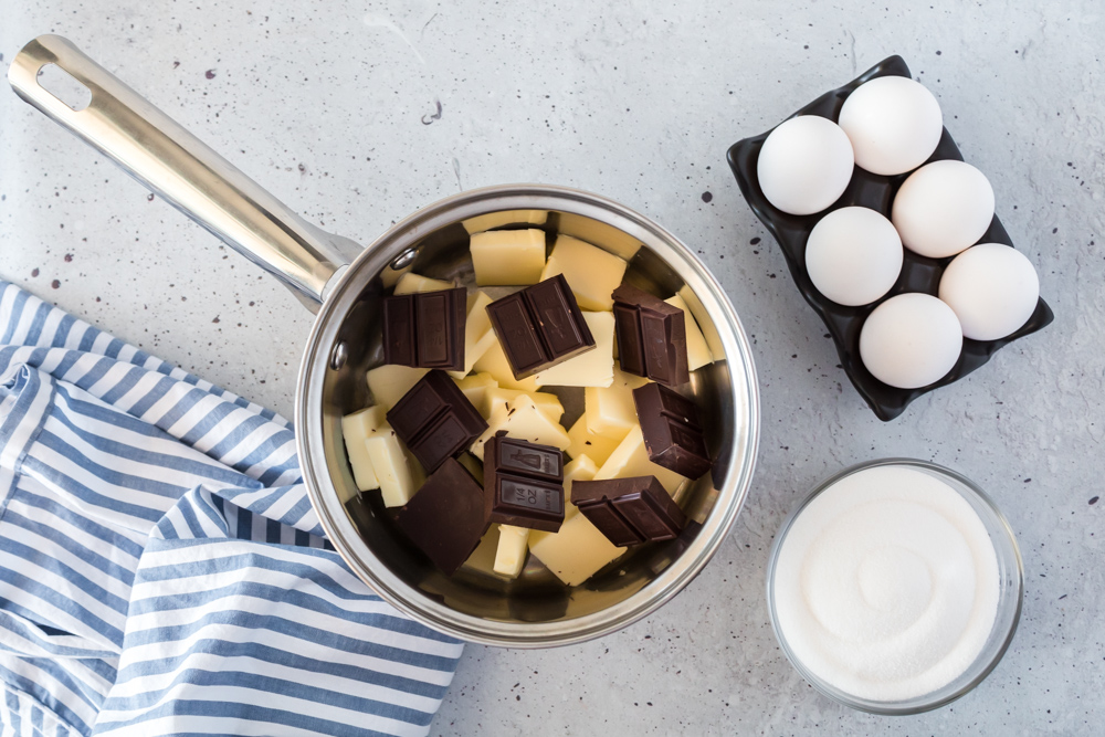 A saucepan with cut butter and chocolate squares with eggs and milk on the side.