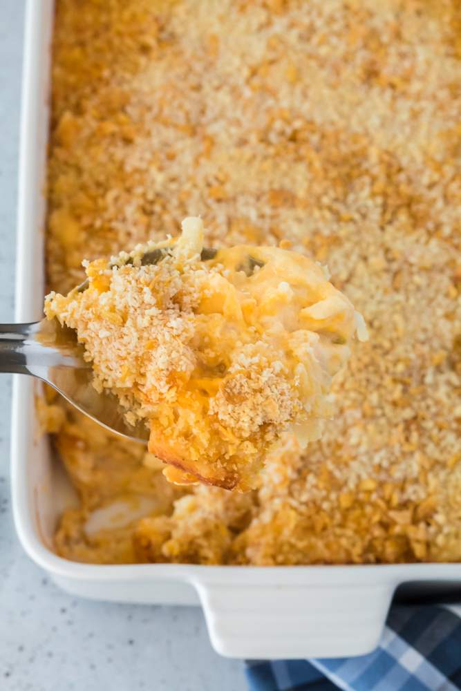 A white pan of potato casserole with a spoon dishing out a serving of it.