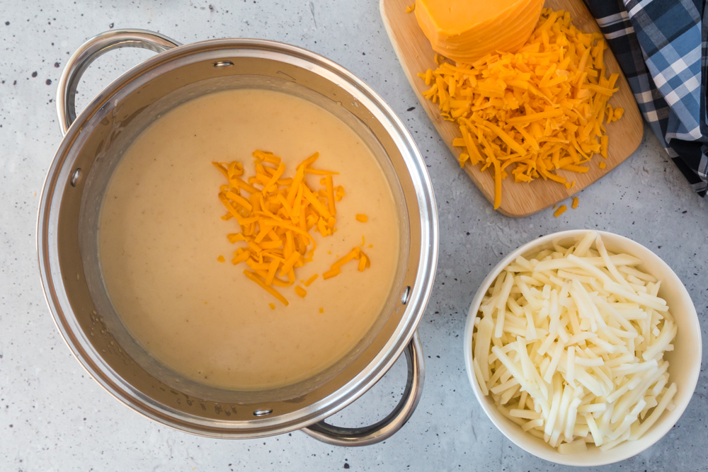 A metal pan with a cheese mixture with shredded cheese in it and on the side of it.