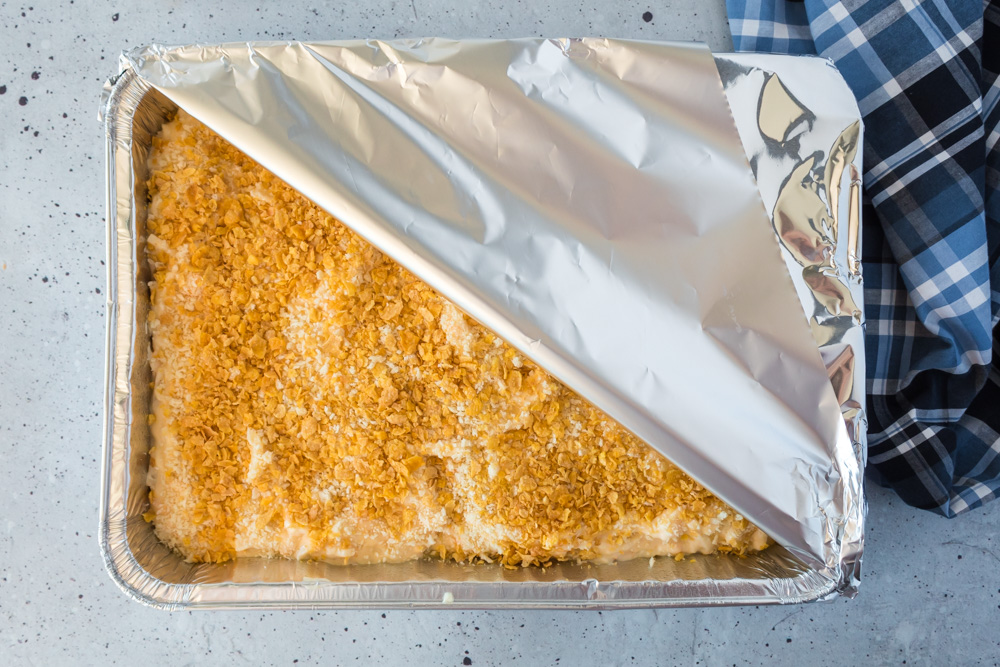 A disposable aluminum pan full of potato casserole with foil over half of it.