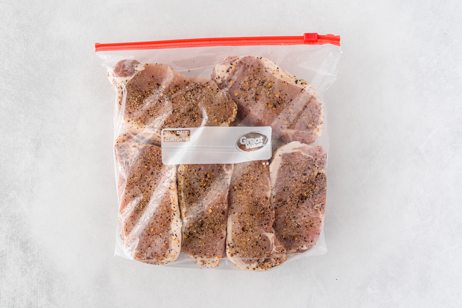 A resealable bag with raw, seasoned pork chops in it.