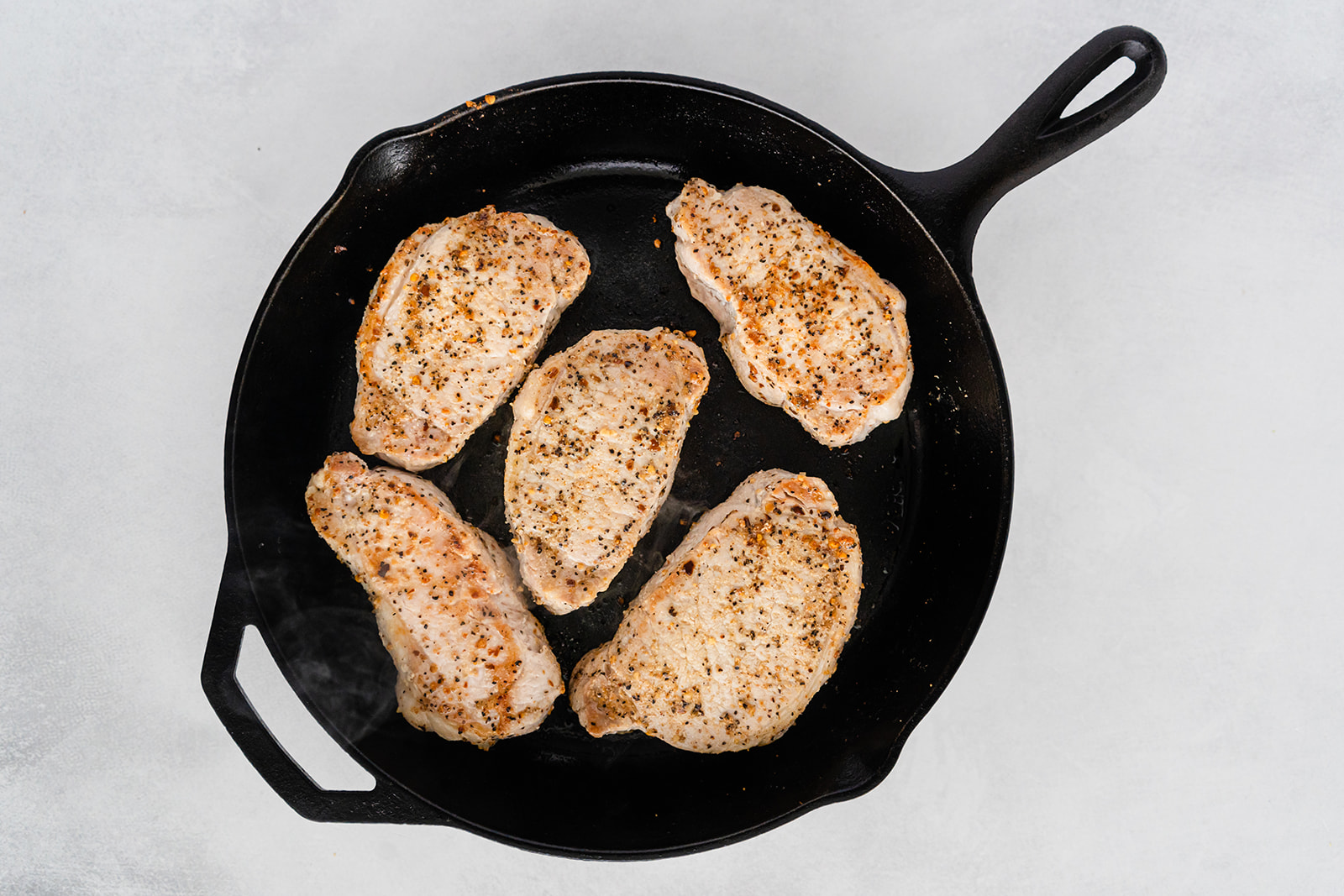 A cast iron pan with cooked, seasoned pork chops on it.
