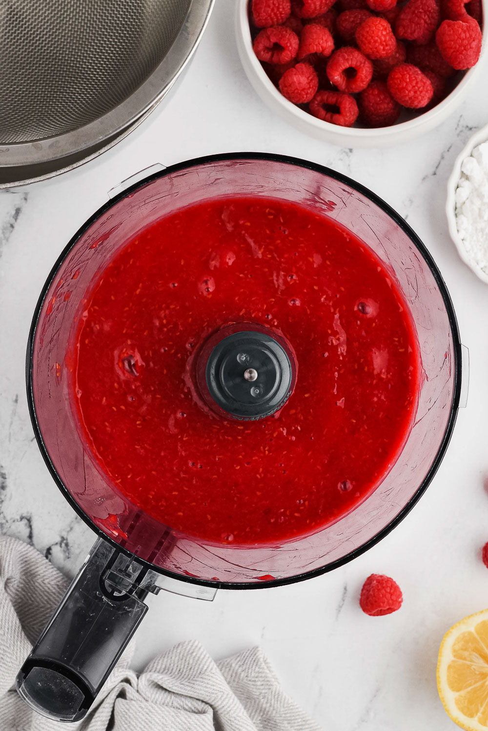 A food processor with fresh raspberry puree in it.