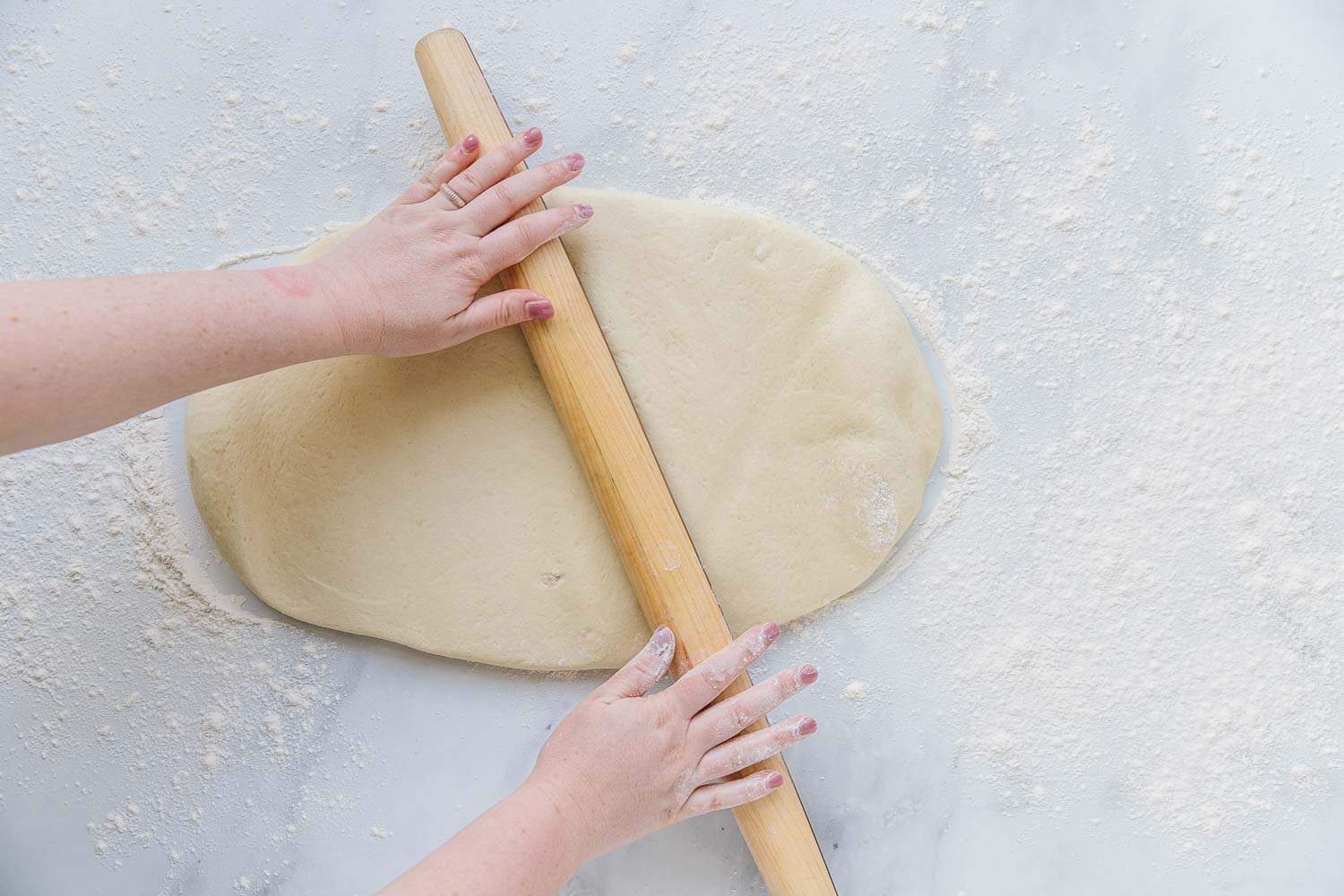 Two hands rolling out dough with a wooden rolling pin.