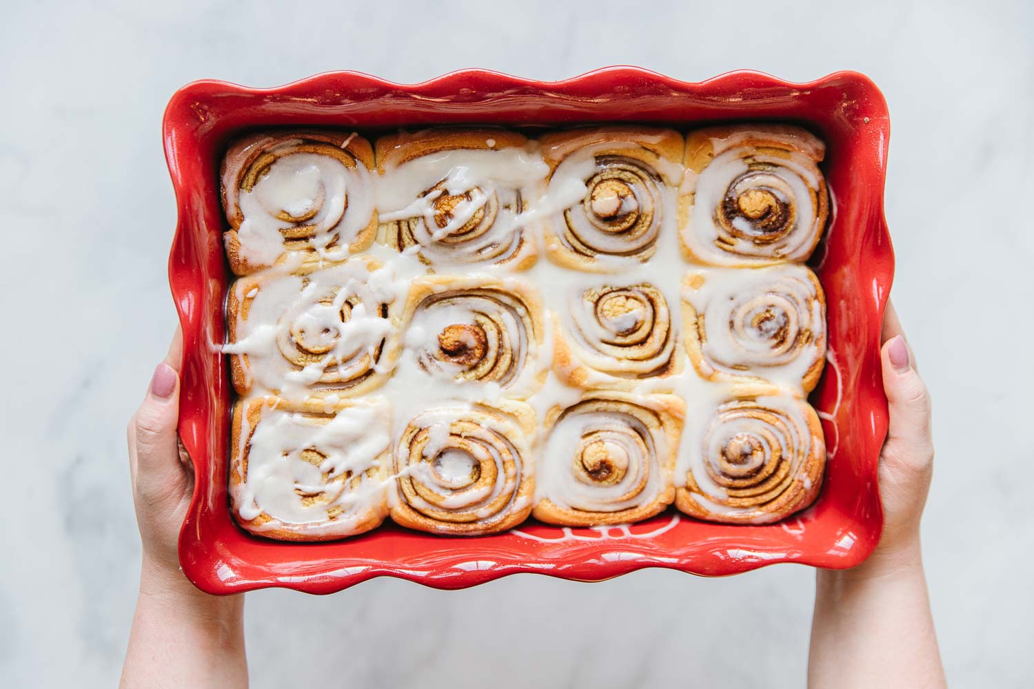 A final pan of iced cinnamon rolls with two hands holding it.