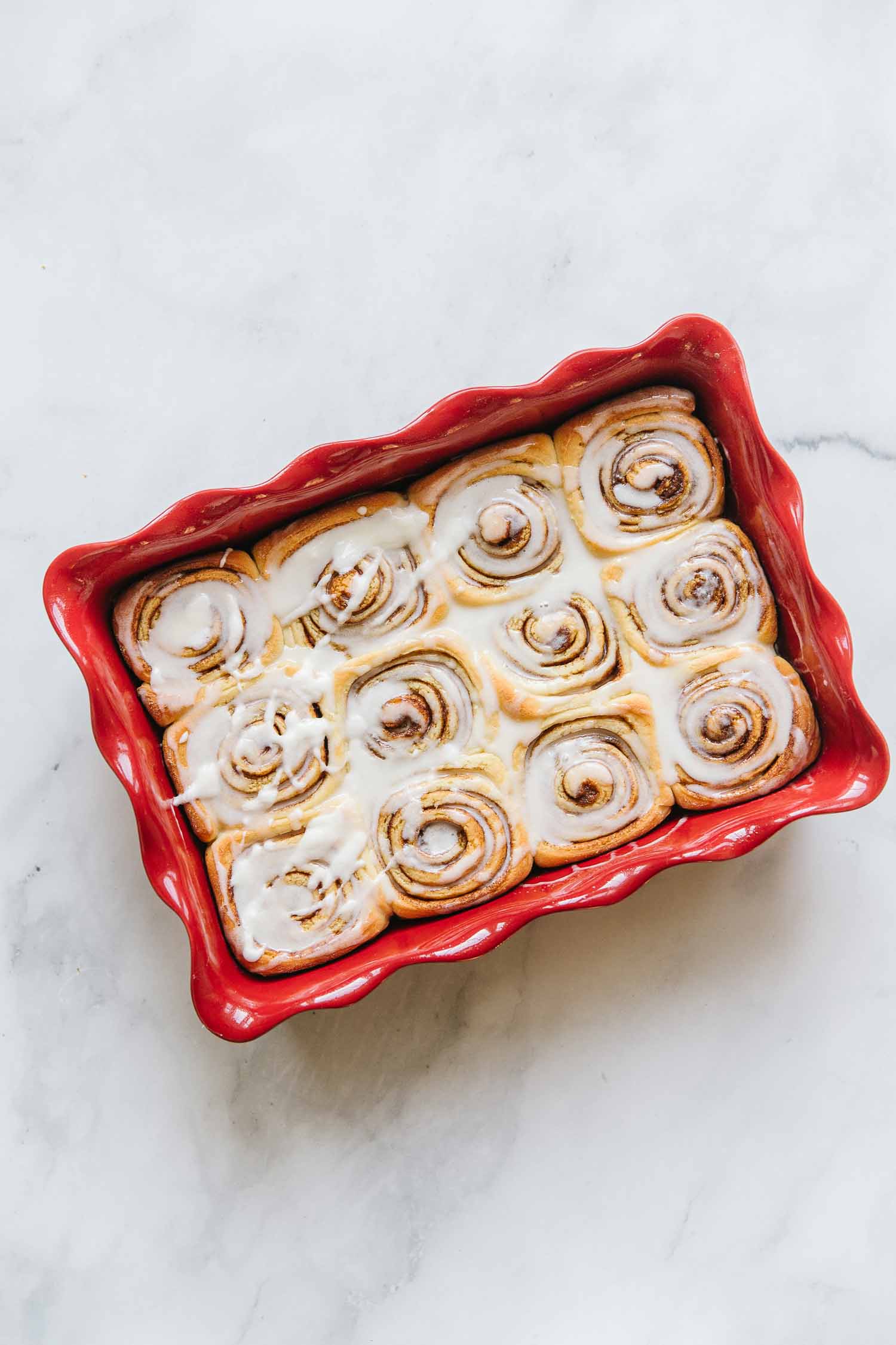 A red pan of cinnamon rolls with icing on it at a diagonal angle.