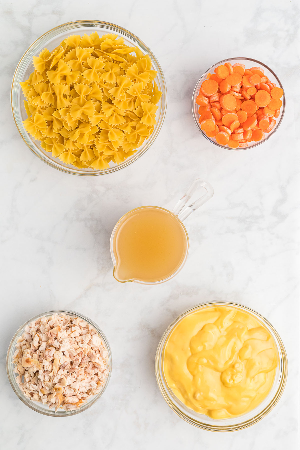 Clear bowls with bowtie pasta, carrots, chicken stock, chicken and cream of chicken soup.
