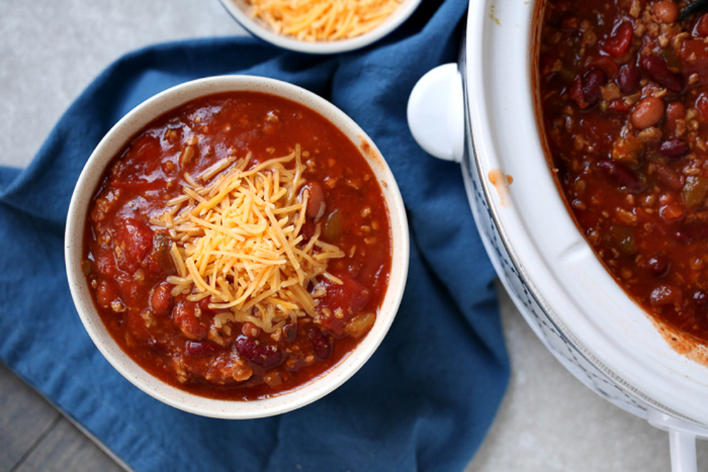 A white bowl of chili and a crockpot of chili next to it.