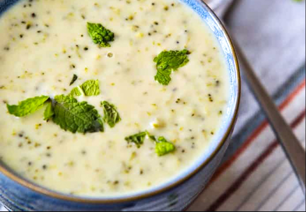 A pottery bowl with cheesy broccoli soup in it with herbs on top of it. 