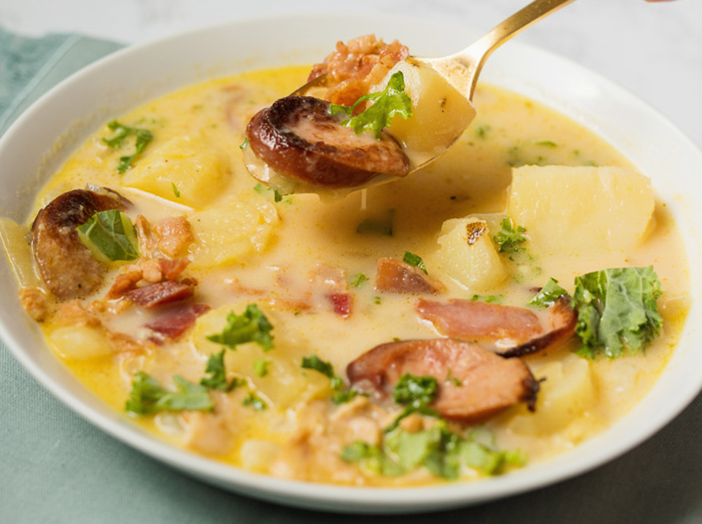 A white bowl of zuppa Toscana soup filled with sausage, spinach and potatoes. 
