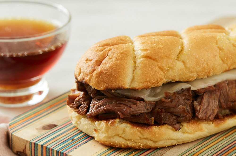 A French dip sandwich with a glass bowl of au jus next to it.
