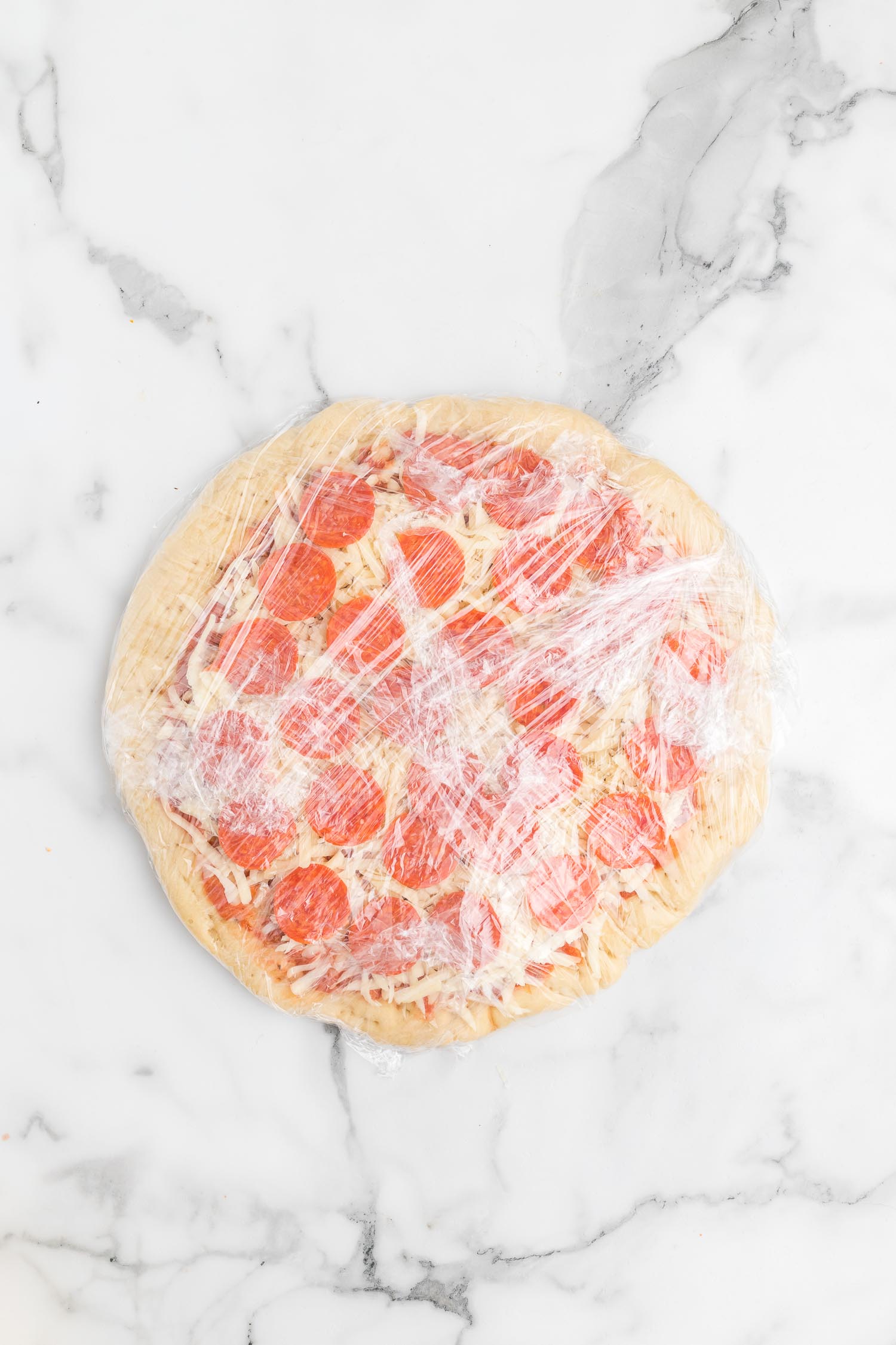 A whole freezer pizza wrapped in plastic wrap.