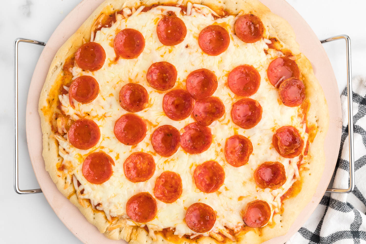 A pizza stone with a whole pepperoni pizza on it.