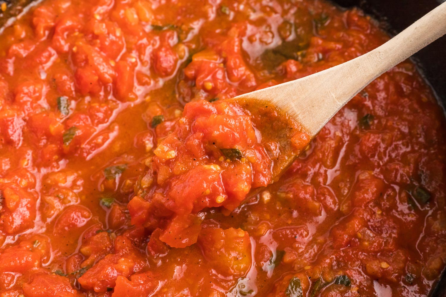 A homemade tomato sauce with a wooden spoon pulling up the sauce.