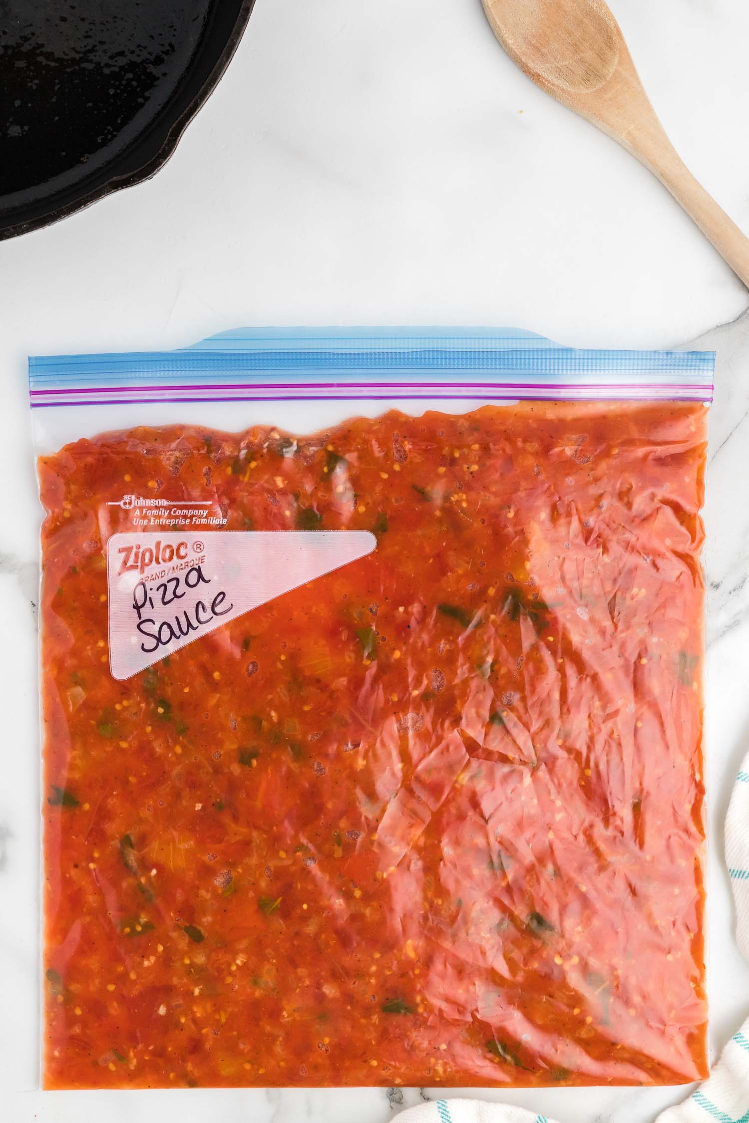 A gallon-size resealable bag with the words "pizza sauce" written in black ink on the bag.