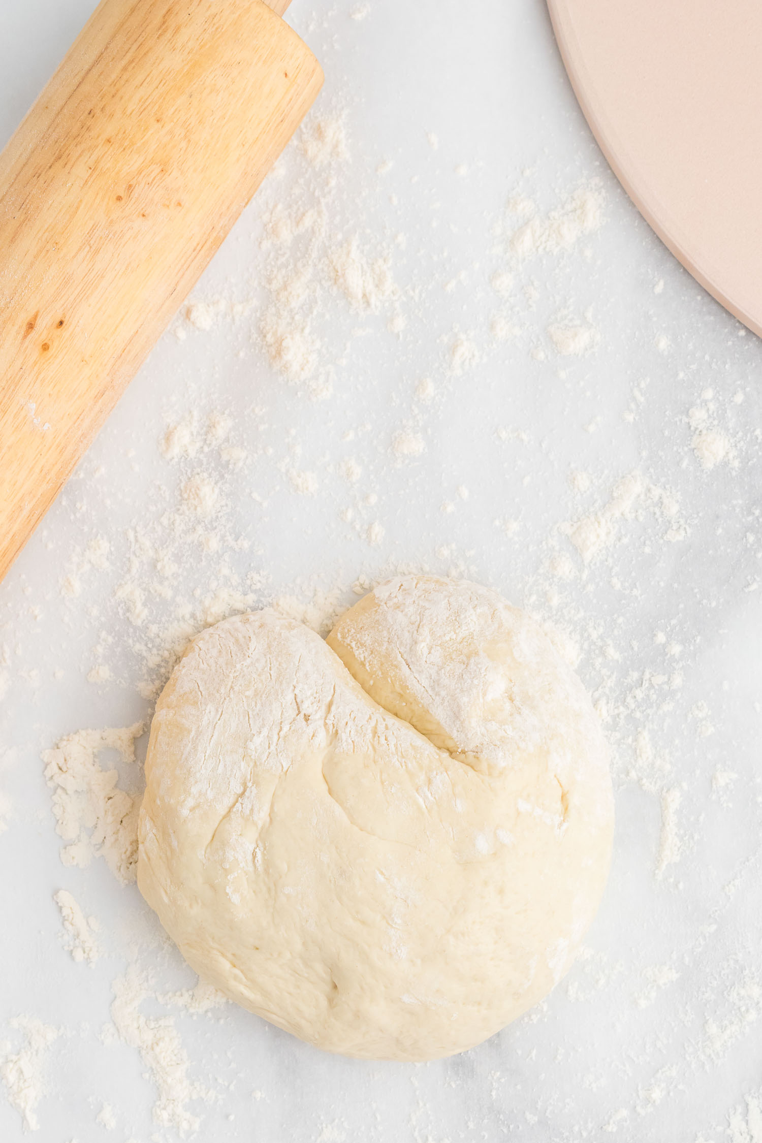 A ball of pizza dough with flour  and a rolling pin and pizza stone next to it.