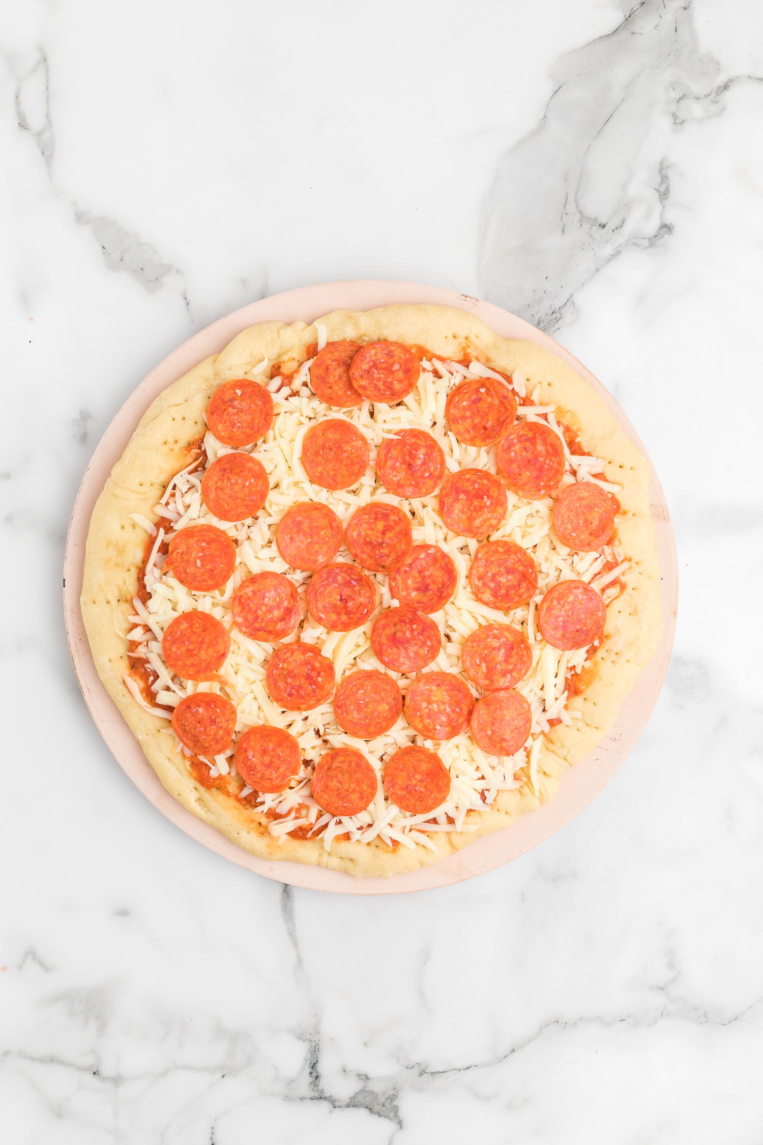 A whole pepperoni pizza on top of a pizza stone on a marble countertop.