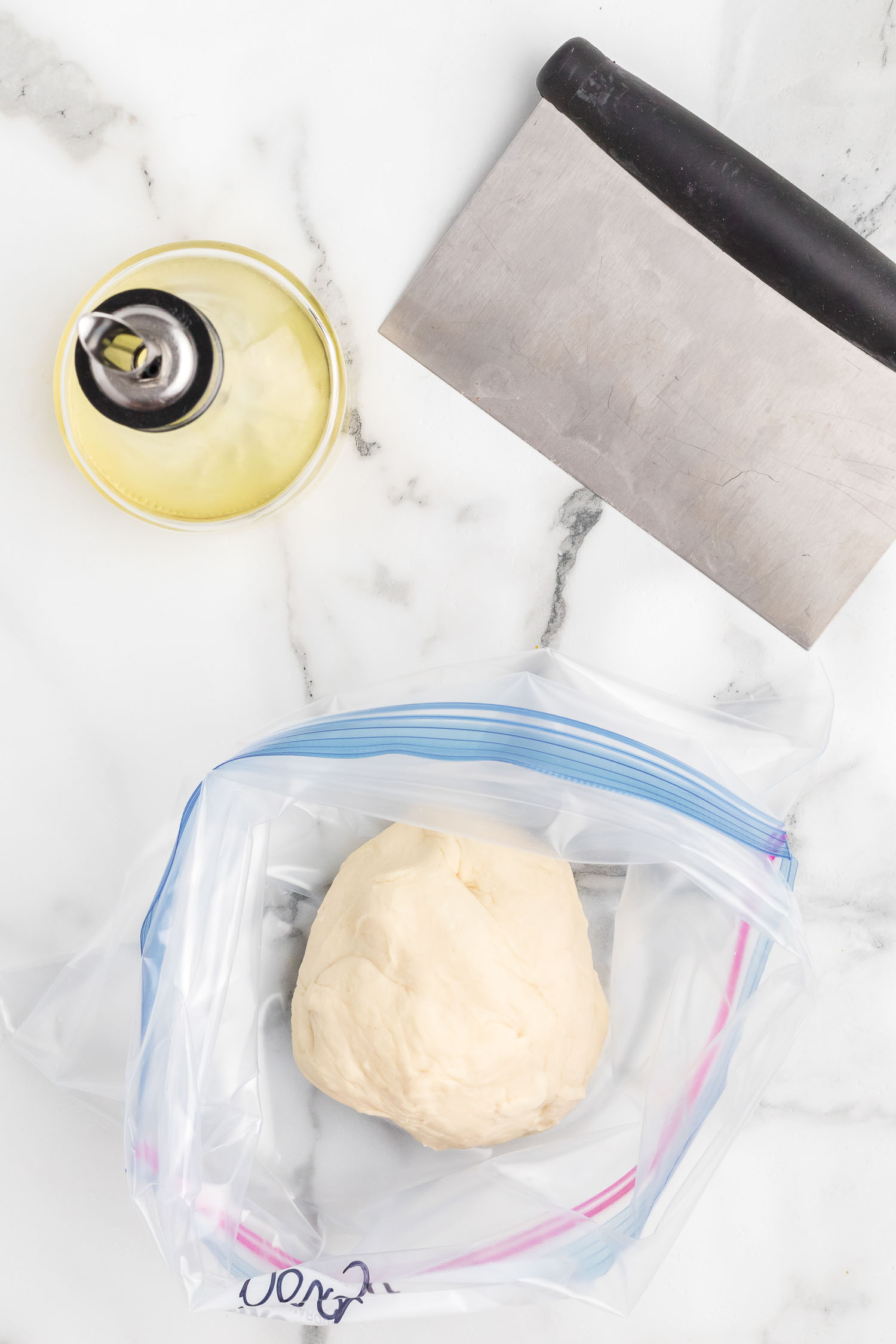 A resealable bag with a ball of dough with oil and a dough cutter.
