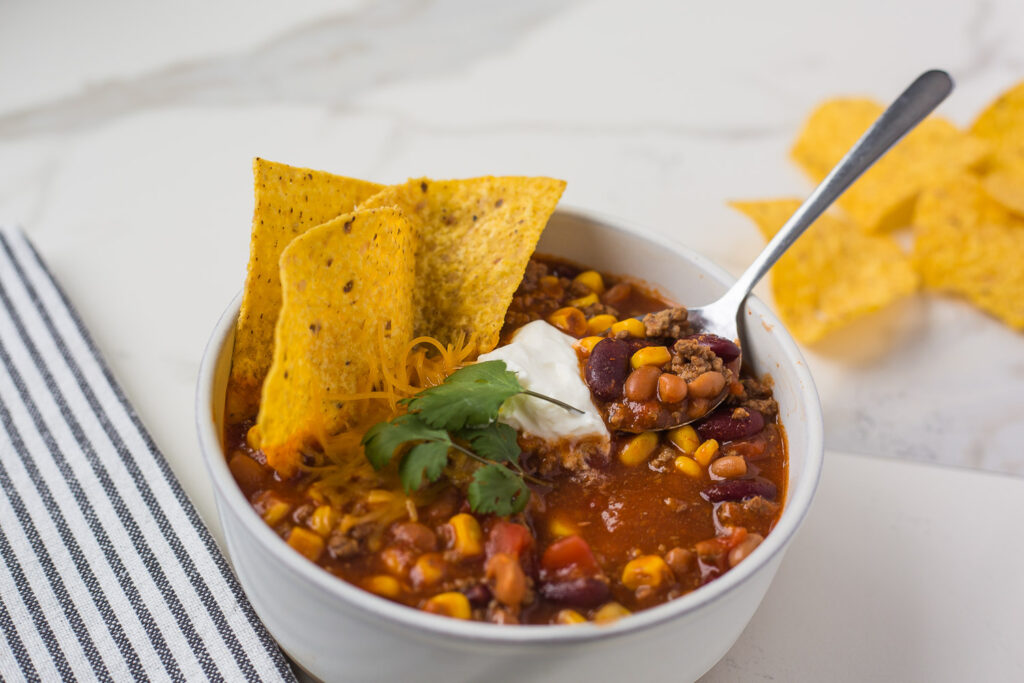 Spoon in a bowl of of taco soup topped with tortilla chips.
