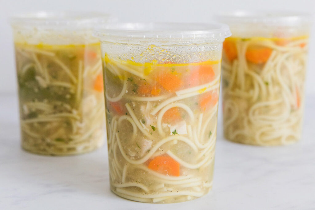 chicken noodle soup in three tall round containers for freezing