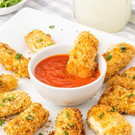 mozzarella sticks arranged on a plate with a marinara bowl in the center.