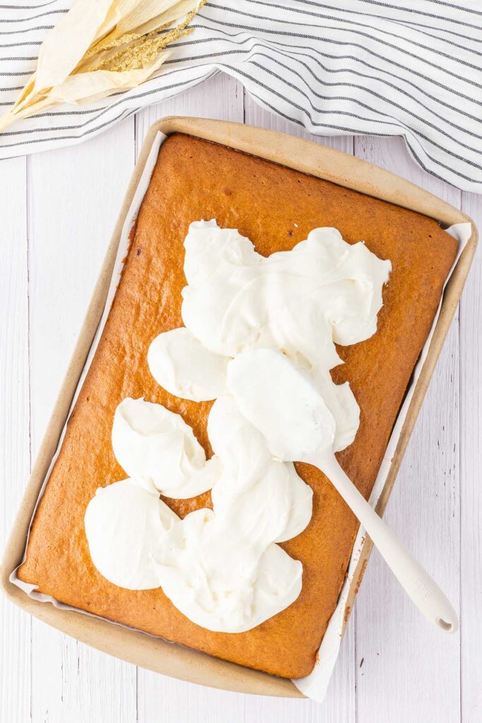spoon spreading cream cheese frosting over the pumpkin cake.
