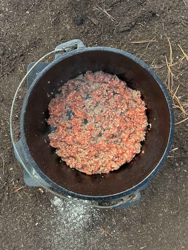 sausage cooking in a dutch oven on charcoal.