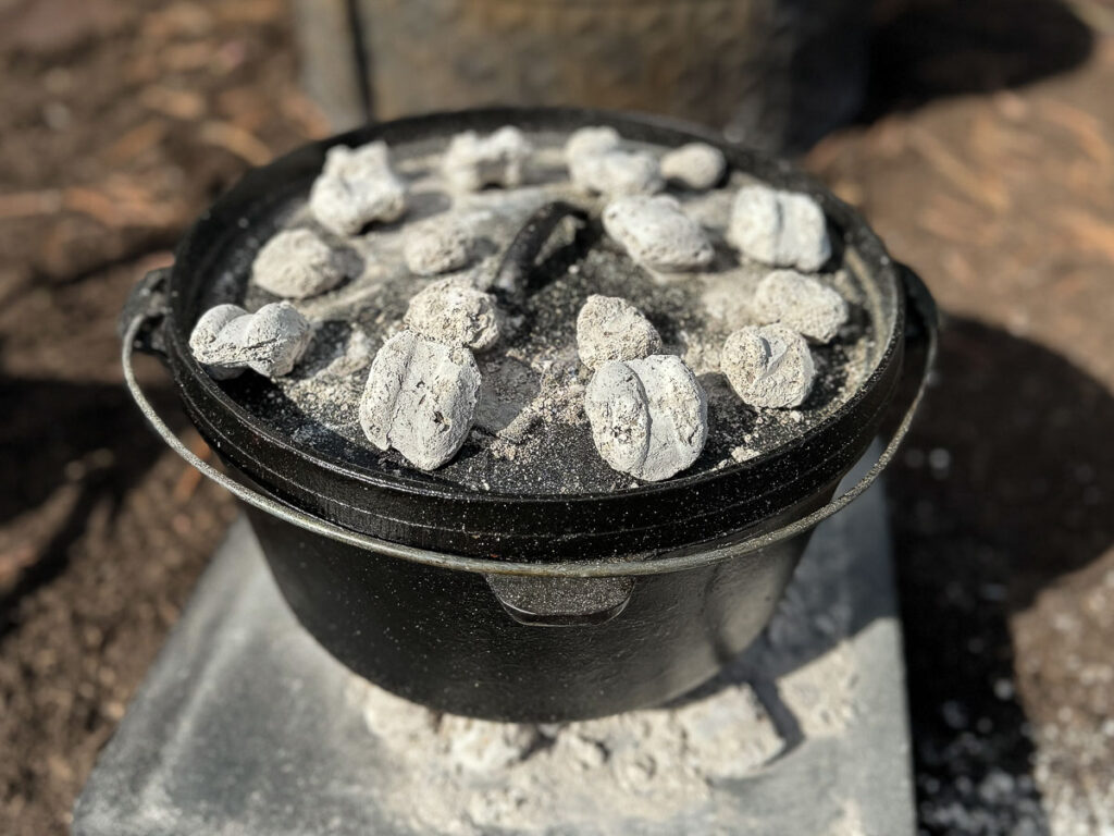 dutch oven is closed and charcoal is added on top.