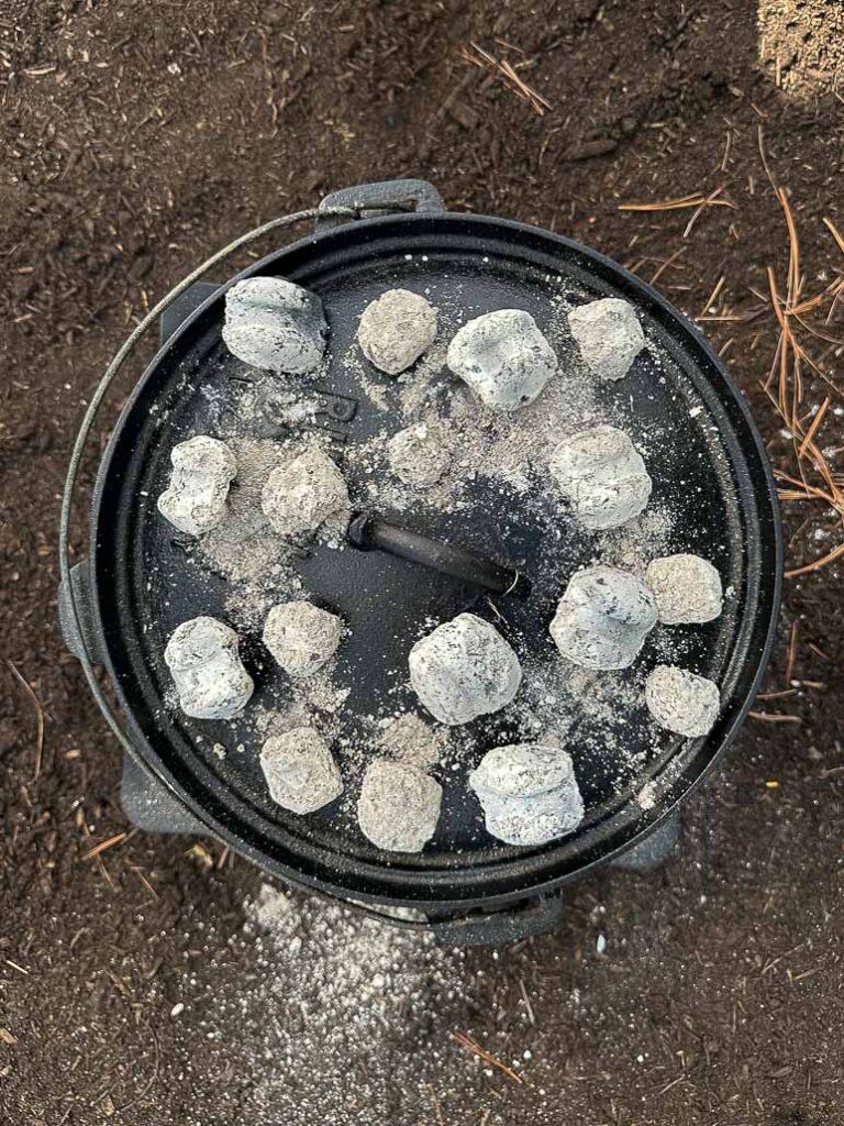 dutch oven is closed and charcoal is added on top.