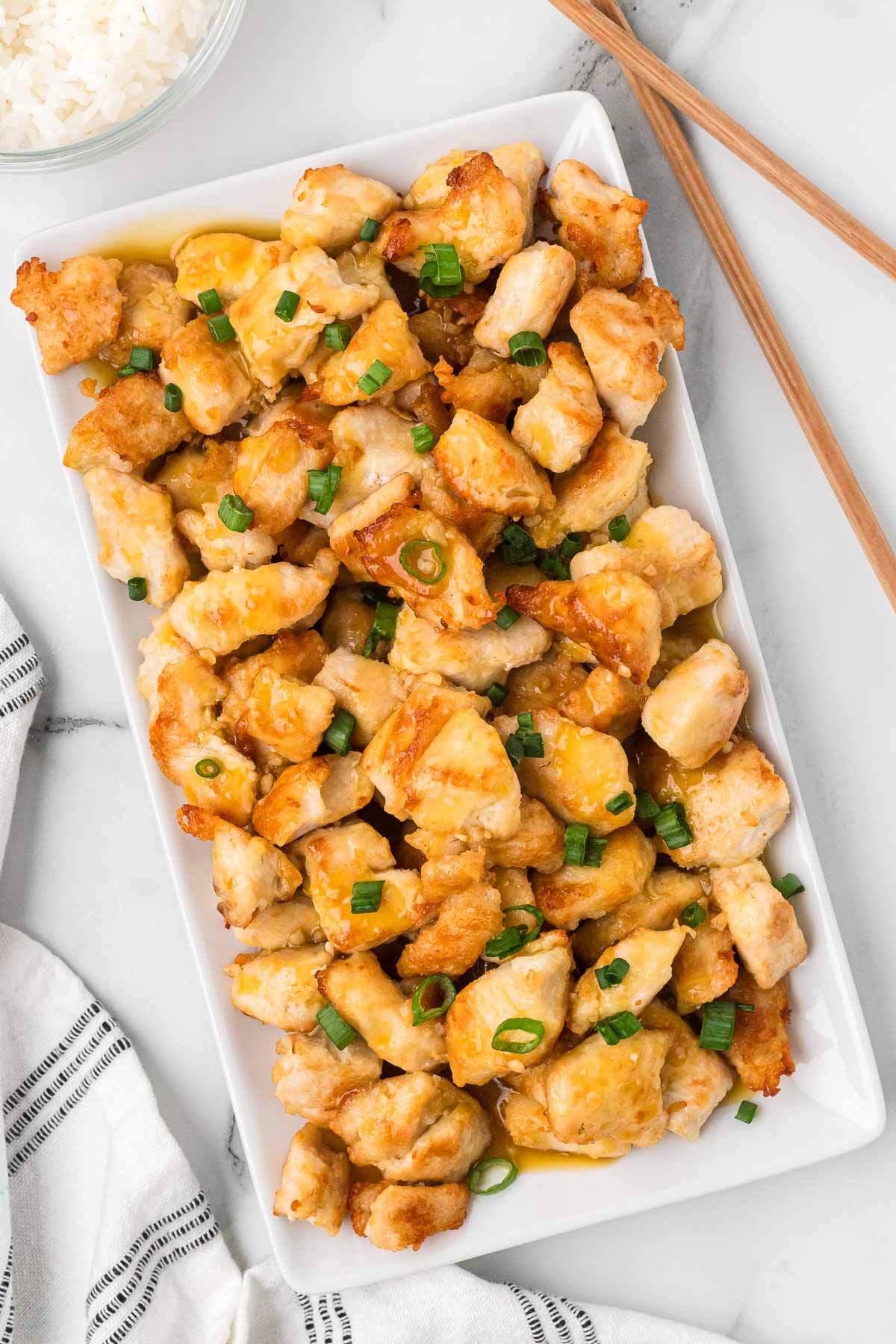 orange chicken on a serving tray topped with green onions.