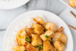 orange chicken on a plate on top of white rice.