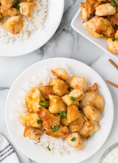 orange chicken on a plate on top of white rice.