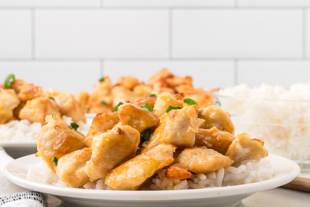 orange chicken on a plate on top of white rice.