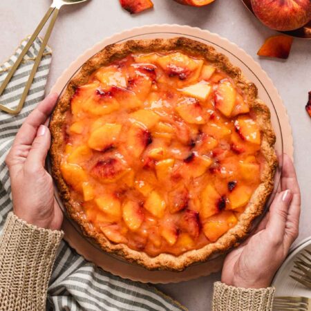 two hands holding a fresh peach pie.