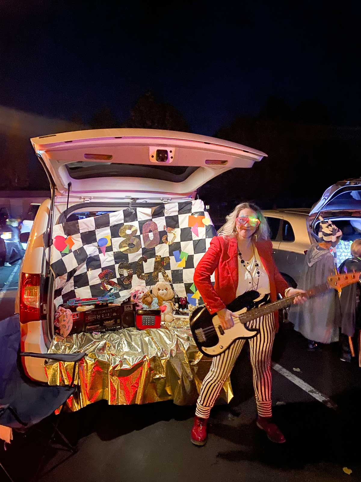 karrie truman in 80's rock clothes next to her 80's style trunk for a halloween trunk or treat.